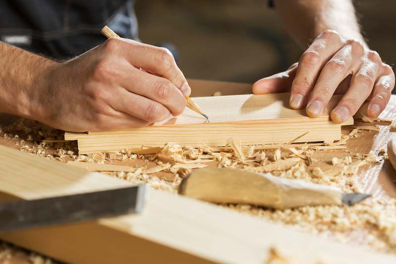 Close-up of hands sanding a wooden cutting board, sawdust visible